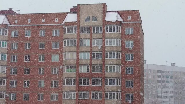 intense snowfall from white large snowflakes against backdrop of multi-storey concrete orange house . Winter fairytale picture at Christmas or new year's Eve. Snow falls slowly and magically.