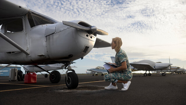 Woman in military uniform checks on a small aviation airplane. Flight pre-check inspection.