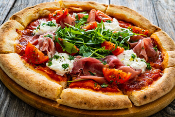 Pizza parma - prosciutto di parma, arugula, mozzarella, tomatoes, burrata on wooden table