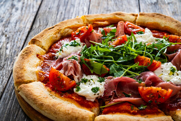 Pizza parma - prosciutto di parma, arugula, mozzarella, tomatoes, burrata on wooden table