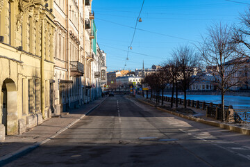 Fototapeta na wymiar Emty street with bare trees on Fontanka river embankment in sunny winter morning in Saint Petersburg city, Russia. River surface covered with ice. Soft focus. Early morning traffic theme.