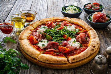 Pizza parma - prosciutto di parma, arugula, mozzarella, tomatoes, burrata on wooden table