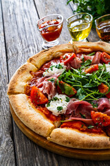 Pizza parma - prosciutto di parma, arugula, mozzarella, tomatoes, burrata on wooden table
