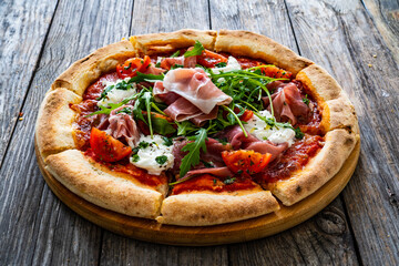 Pizza parma - prosciutto di parma, arugula, mozzarella, tomatoes, burrata on wooden table