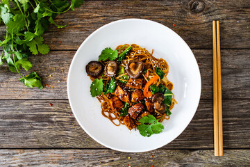 Asian food - chicken nuggets, noodles, stir fried vegetables, soy sauce, pak choi cabbage and shiitake mushrooms on wooden table 