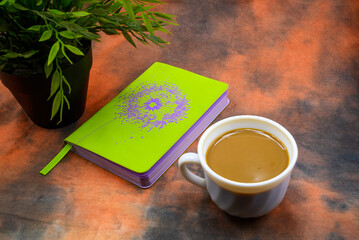 green notebook and a green flower in a pot next to a cup of coffee