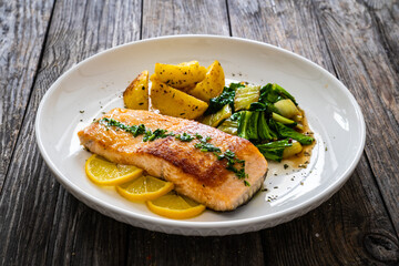 Fried salmon steak with lemon, fried potatoes and pak choi cabbage served on wooden table
