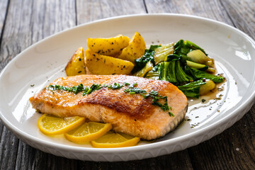 Fried salmon steak with lemon, fried potatoes and pak choi cabbage served on wooden table
