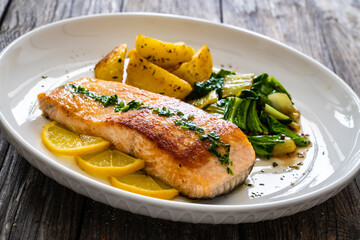 Fried salmon steak with lemon, fried potatoes and pak choi cabbage served on wooden table
