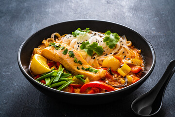 Tom Yum - Thai soup with salmon and rice noodles on wooden table
