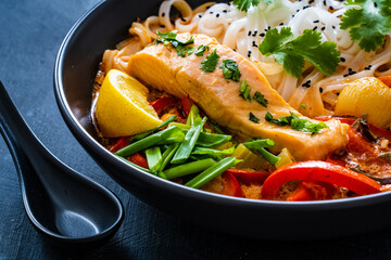 Tom Yum - Thai soup with salmon and rice noodles on wooden table
