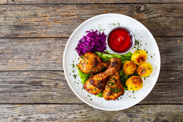 Barbecue chicken drumsticks with fried potatoes, lettuce and ketchup on wooden table
