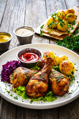 Barbecue chicken drumsticks with fried potatoes, lettuce and ketchup on wooden table
