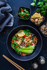 Asian food - chicken nuggets, noodles, stir fried vegetables, soy sauce, pak choi cabbage  and shiitake mushrooms on wooden table

