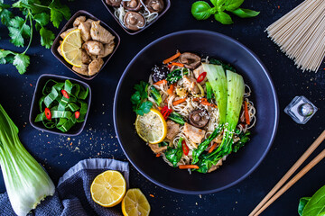 Asian food - chicken nuggets, noodles, stir fried vegetables, soy sauce, pak choi cabbage  and shiitake mushrooms on wooden table

