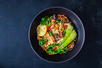 Asian food - chicken nuggets, noodles, stir fried vegetables, soy sauce, pak choi cabbage  and shiitake mushrooms on wooden table
