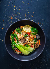 Asian food - chicken nuggets, noodles, stir fried vegetables, soy sauce, pak choi cabbage  and shiitake mushrooms on wooden table
