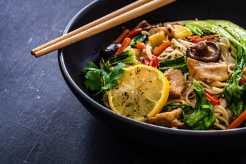 Asian food - chicken nuggets, noodles, stir fried vegetables, soy sauce, pak choi cabbage  and shiitake mushrooms on wooden table
