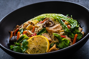 Asian food - chicken nuggets, noodles, stir fried vegetables, soy sauce, pak choi cabbage  and shiitake mushrooms on wooden table
