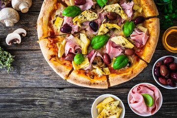 Pizza capricciosa with cooked ham, mozzarella, artichoke   and vegetables on wooden table
