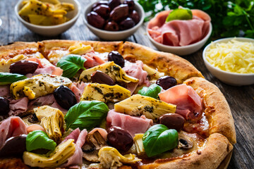 Pizza capricciosa with cooked ham, mozzarella, artichoke   and vegetables on wooden table
