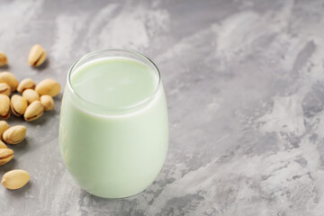 Organic non dairy pistachio milk in glass with pistachionuts on gray background. Vegan plant based milk. Copy space