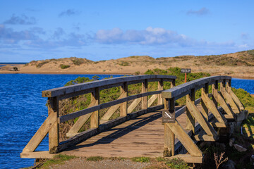 Wooden foot bridge with no cycling sign over blue water by dry sand dunes