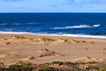 Fototapeta na wymiar Small waves break on deserted sandy beach with blue water to the horizon