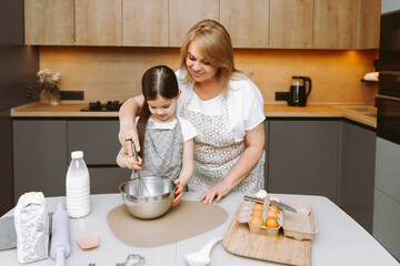 Obraz na płótnie Canvas Caring grandmother and little granddaughter are having fun baking cookies together in the home kitchen. A loving elderly grandmother and granddaughter prepare a delicious sweet cake.