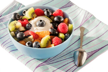 Freshly prepared delicious healthy fruit salad for breakfast in a blue ceramic bowl. White isolated background.