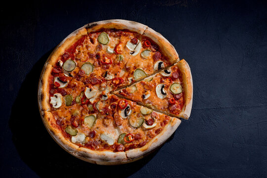 Appetizing pizza with hunting sausages, mozzarella cheese, pickled cucumbers, chili peppers on a tomato base on black background