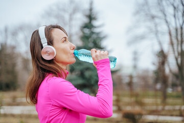 An athletic woman running on a trail in taking a moment to drink water from her bottle