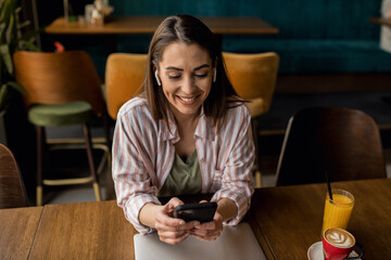 Beautiful woman with wireless headphones, sitting in a restaurant using her phone