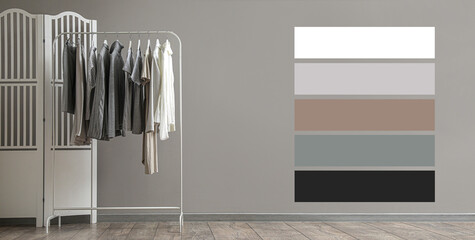 Rack with stylish female clothes and folding screen near grey wall. Different color patterns