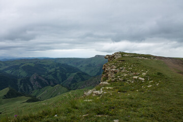 Fototapeta premium Panoramic view of green mountains and hills and a haze from the Bermamyt plateau in Karachay-Cherkessia in Russia on a cloudy summer day and a space for copy