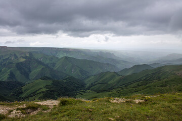Panoramic view of green mountains and hills and a haze from the Bermamyt plateau in Karachay-Cherkessia in Russia on a cloudy summer day and a space for copy