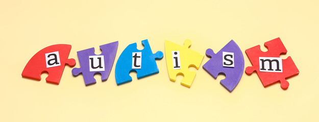 Word AUTISM and jigsaw puzzle pieces on beige background