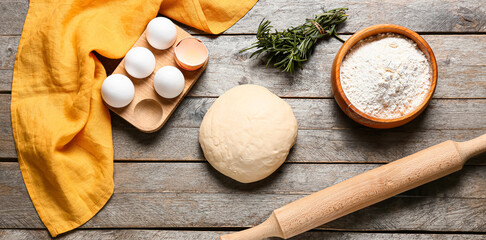 Fresh dough, flour, eggs, rolling pin and rosemary on wooden background