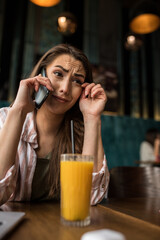 A young woman cries over a phone call while sitting alone in a café