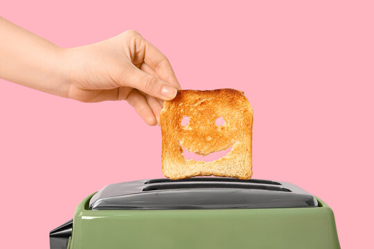 Woman taking funny bread slice from modern toaster on pink background