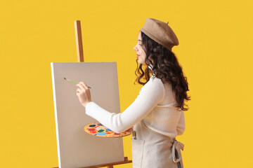 Fototapeta Teenage artist with brush and paint palette drawing on yellow background obraz