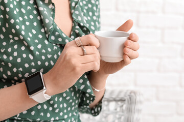 Woman with smartwatch and cup of coffee at home, closeup