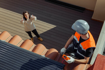 Top view of Happy female customer owner of the house with thumbs up while worker installs solar...