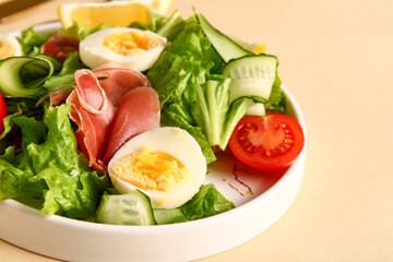 Plate of delicious salad with boiled eggs and jamon on beige background, closeup