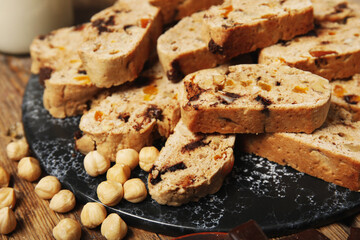 Board with delicious biscotti cookies and hazelnuts on wooden background
