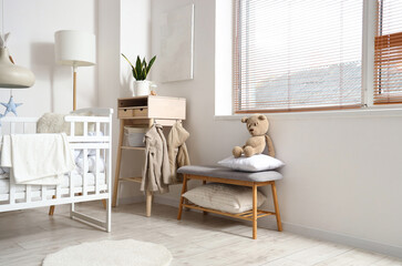 Interior of light children's bedroom with baby crib, table and bench