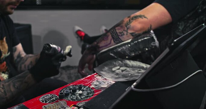 Close up tattoo artist shows the process of getting black tattoos with paint. The master works in black sterile gloves. Master tattoo artist in studio.