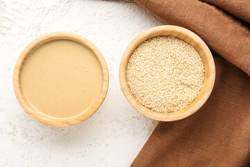 Wooden bowls with tasty tahini and sesame seeds on light background