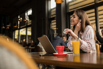 Woman putting in wireless earphones while working remotely from a restaurant