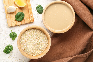 Composition with bowls of tasty tahini, sesame seeds, garlic and spinach on light background, closeup